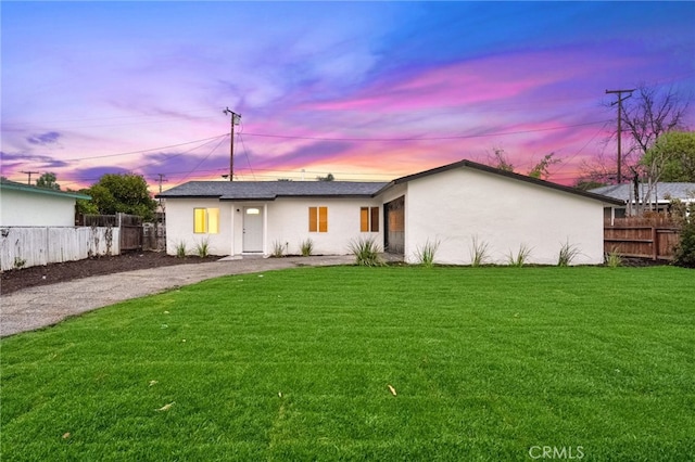 back of house at dusk featuring stucco siding, a lawn, and fence