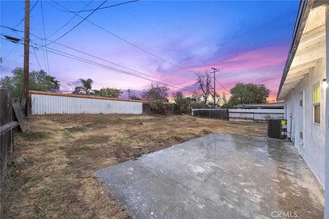 yard at dusk with central AC, a fenced backyard, and a patio area