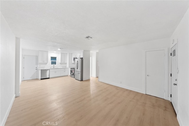 unfurnished living room with light wood-style floors, visible vents, and baseboards