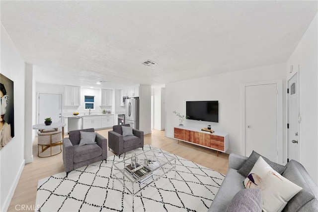 living area featuring a textured ceiling, baseboards, visible vents, and light wood-type flooring