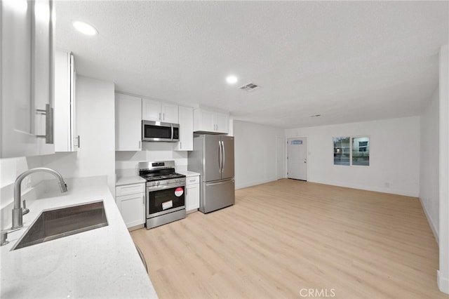 kitchen featuring visible vents, light wood-style flooring, stainless steel appliances, white cabinetry, and a sink