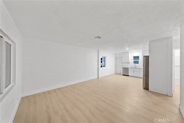 unfurnished living room with light wood-type flooring, visible vents, a sink, a textured ceiling, and baseboards