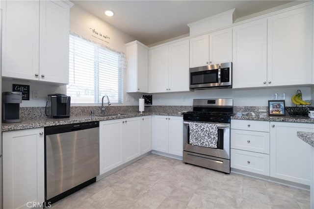 kitchen featuring a sink, stainless steel appliances, white cabinets, and dark stone countertops