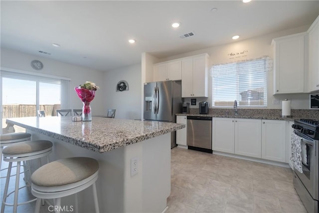 kitchen featuring visible vents, appliances with stainless steel finishes, a breakfast bar, and light stone countertops