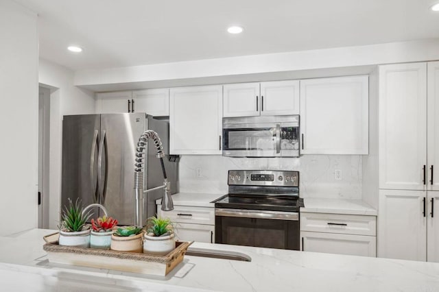 kitchen featuring backsplash, appliances with stainless steel finishes, white cabinetry, and light stone countertops