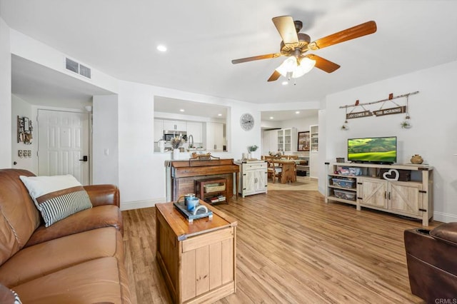 living room featuring visible vents, light wood-type flooring, and a ceiling fan