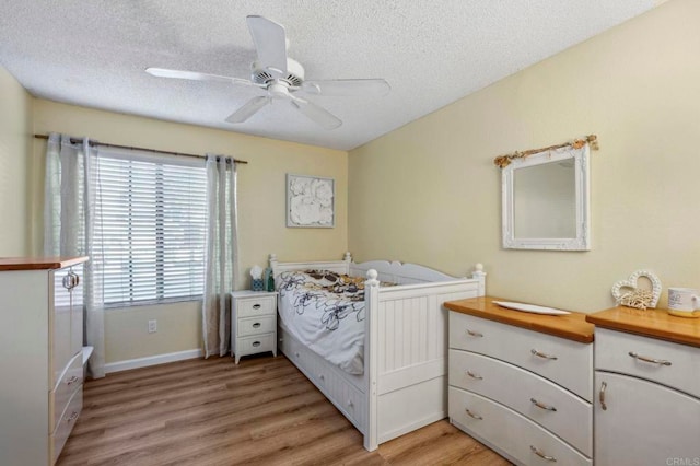 bedroom featuring baseboards, a textured ceiling, light wood-style flooring, and a ceiling fan