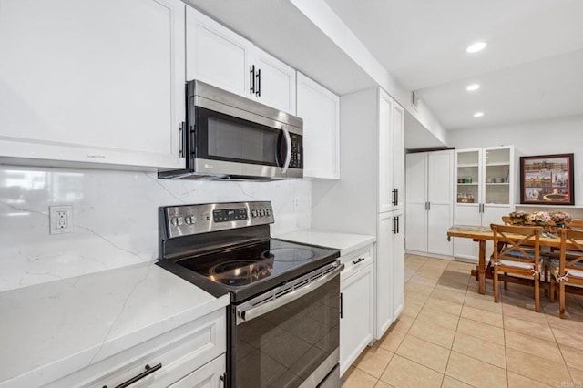 kitchen with light stone counters, white cabinetry, stainless steel appliances, light tile patterned floors, and decorative backsplash