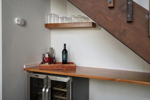 interior details featuring wine cooler, a dry bar, and a textured wall