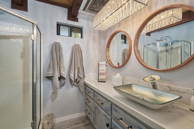 full bath featuring a shower stall, baseboards, wood finished floors, a notable chandelier, and vanity