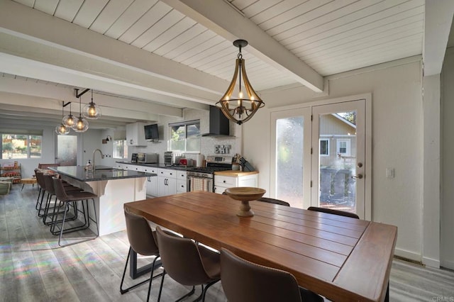 dining area with light wood-type flooring, beam ceiling, a notable chandelier, and baseboards