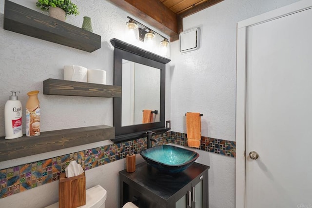 half bath with vanity, toilet, a textured wall, and backsplash