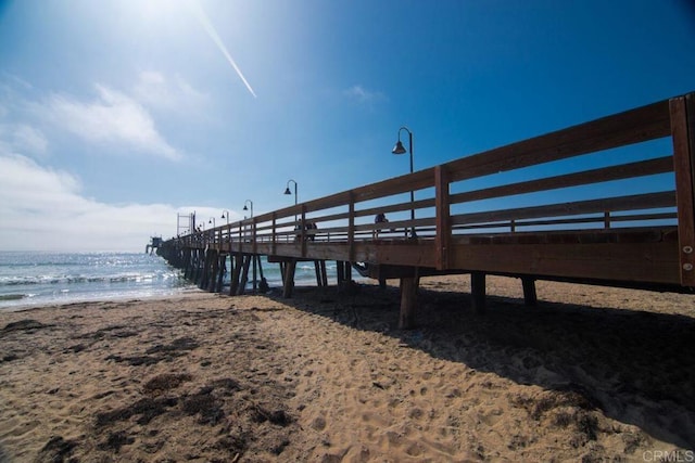 dock area with a pier, a water view, and a beach view