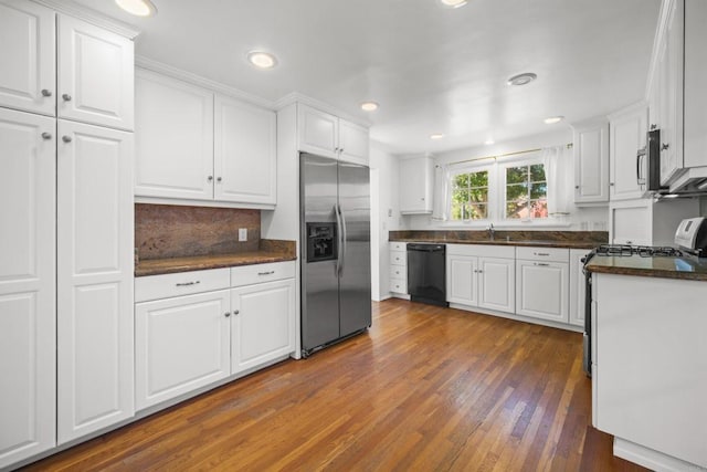 kitchen with white cabinets, appliances with stainless steel finishes, a sink, hardwood / wood-style floors, and backsplash