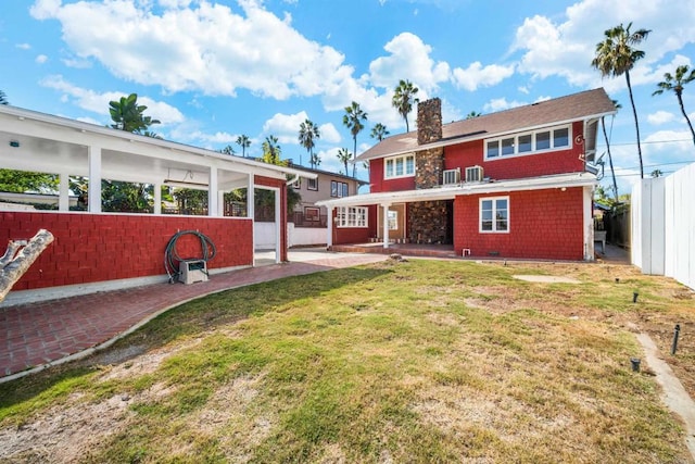 back of house with a patio area, a lawn, fence, and a chimney