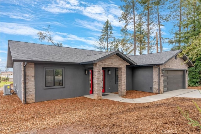 view of front of property featuring central AC unit, roof with shingles, concrete driveway, stone siding, and a garage