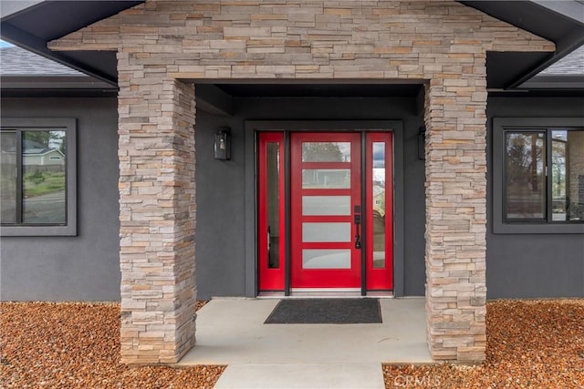 doorway to property featuring a shingled roof, stone siding, and stucco siding