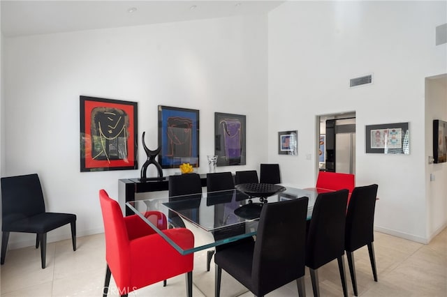 dining space with light tile patterned floors, visible vents, baseboards, and a high ceiling