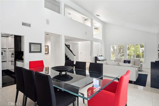 dining area with light tile patterned floors, visible vents, high vaulted ceiling, and stairs