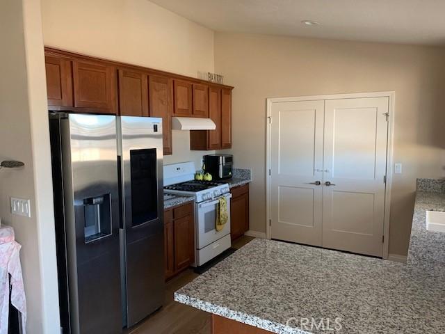 kitchen with under cabinet range hood, gas range gas stove, brown cabinetry, and stainless steel refrigerator with ice dispenser