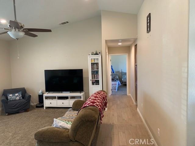 living area featuring light wood-type flooring, visible vents, baseboards, ceiling fan, and vaulted ceiling