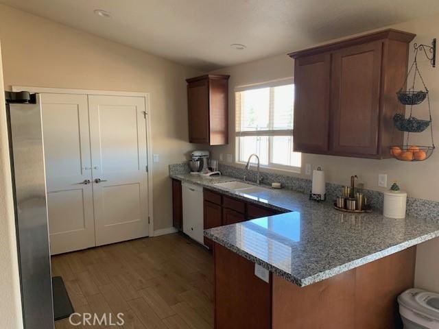 kitchen featuring light wood-style flooring, a sink, light stone counters, a peninsula, and white dishwasher