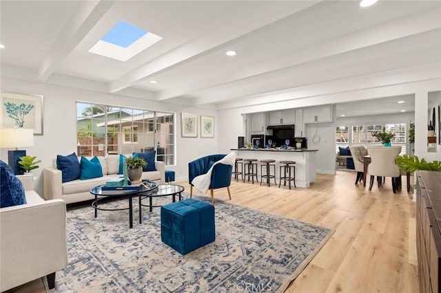 living area featuring baseboards, beam ceiling, recessed lighting, a skylight, and light wood-style floors