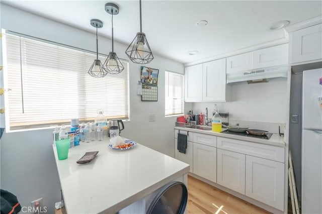 kitchen with freestanding refrigerator, white cabinets, light countertops, and under cabinet range hood