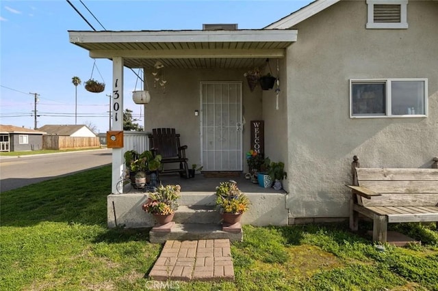 property entrance featuring covered porch, stucco siding, and a lawn