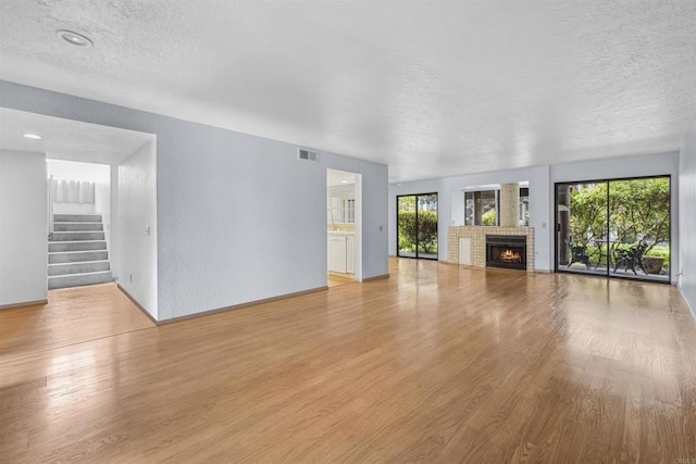 unfurnished living room featuring stairway, visible vents, light wood finished floors, a fireplace, and a textured ceiling