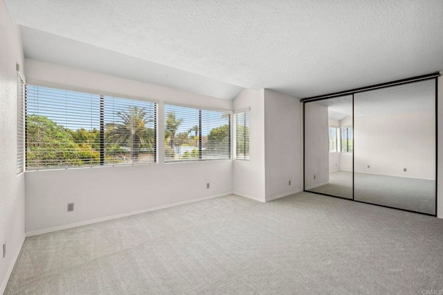 unfurnished bedroom with carpet flooring, lofted ceiling, multiple windows, and a textured ceiling