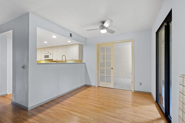 interior space with a ceiling fan, white microwave, light wood-type flooring, and french doors