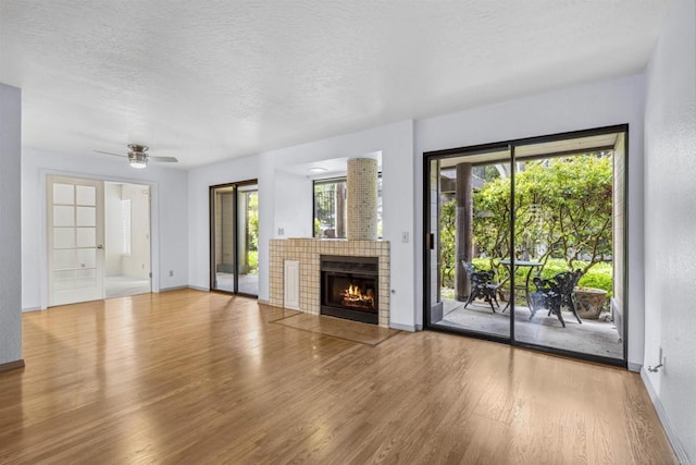 unfurnished living room with a wealth of natural light, a textured ceiling, wood finished floors, and a tiled fireplace