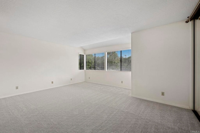 unfurnished room with baseboards, a textured ceiling, lofted ceiling, and carpet