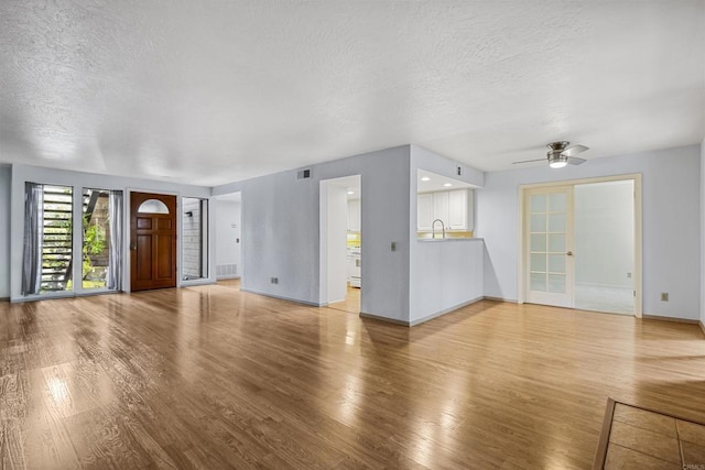 unfurnished living room featuring baseboards, visible vents, light wood-style flooring, ceiling fan, and a textured ceiling