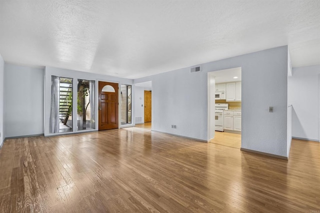 unfurnished living room featuring a textured ceiling, baseboards, visible vents, and light wood-type flooring