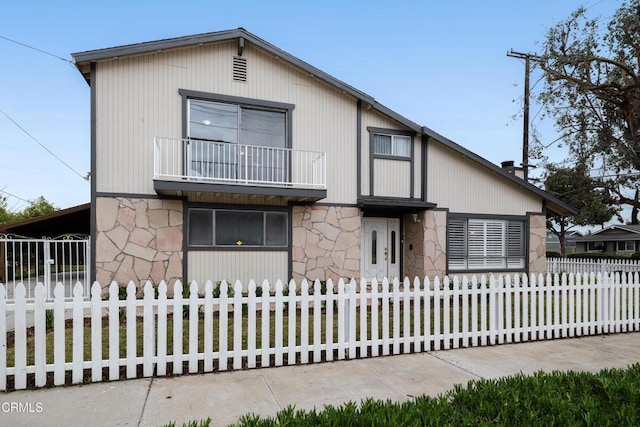 view of front facade with a fenced front yard, stone siding, and a balcony