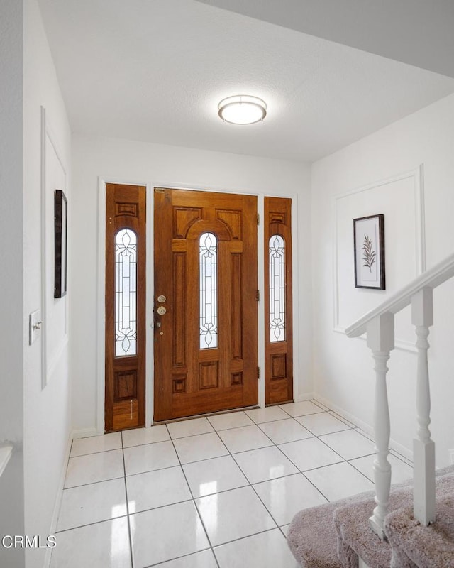 foyer featuring light tile patterned floors, baseboards, and stairs