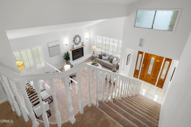 stairway with tile patterned floors, high vaulted ceiling, and a glass covered fireplace