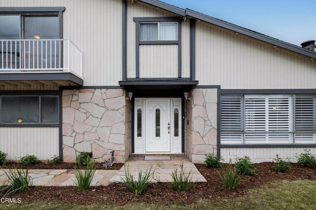 property entrance with stone siding and a balcony