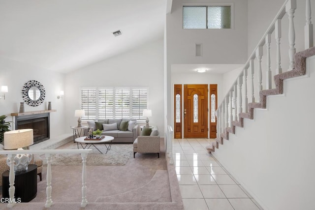 tiled entryway with visible vents, high vaulted ceiling, a fireplace with raised hearth, and stairs