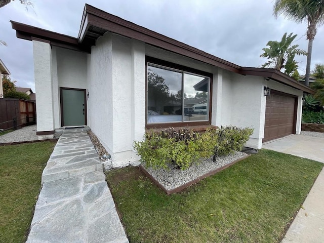 view of front of home featuring a front yard, fence, an attached garage, stucco siding, and concrete driveway