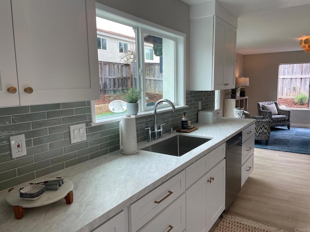 kitchen with tasteful backsplash, light wood finished floors, light countertops, dishwashing machine, and a sink