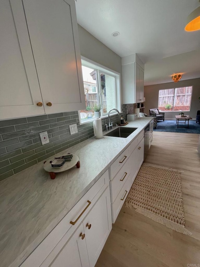 kitchen with a sink, light wood-type flooring, tasteful backsplash, and white cabinetry