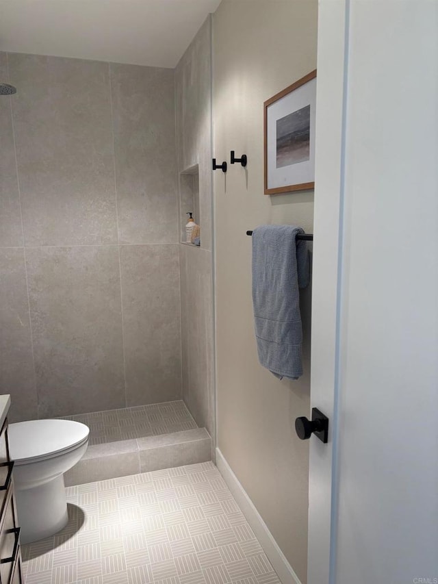 full bath featuring a tile shower, toilet, vanity, and baseboards