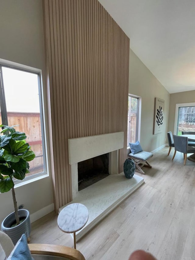 living room featuring wood finished floors, baseboards, a wealth of natural light, and a fireplace with raised hearth