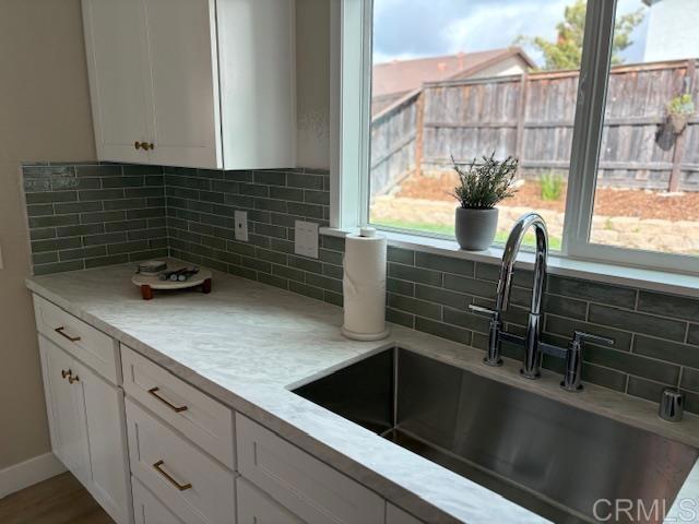 kitchen with a sink, backsplash, light countertops, and white cabinetry