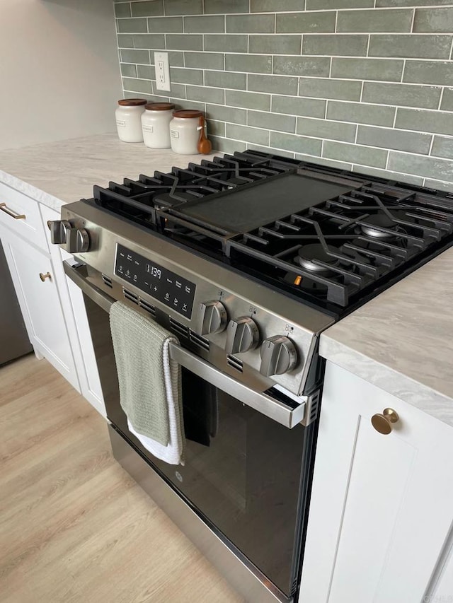 room details with stainless steel gas stove, backsplash, light wood-style floors, white cabinets, and light countertops