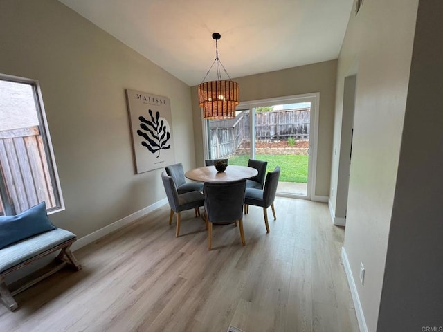 dining space with an inviting chandelier, light wood-style floors, baseboards, and lofted ceiling