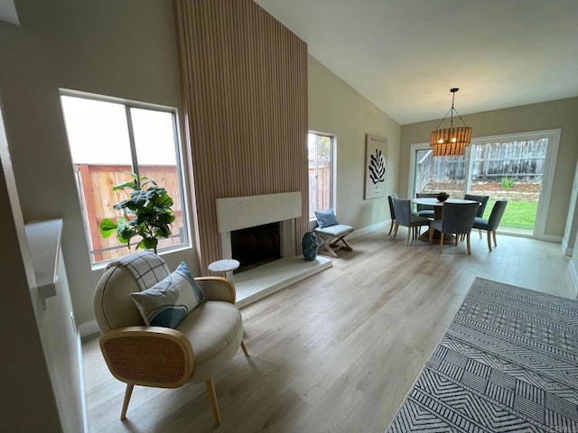 living area with baseboards, light wood-type flooring, a fireplace, an inviting chandelier, and high vaulted ceiling